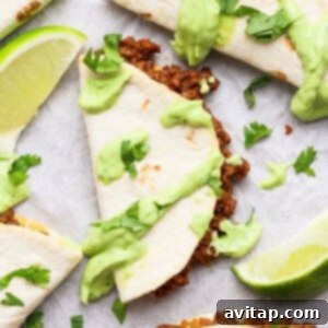 Taco halves with ground meat filling, topped with green sauce and cilantro, served with lime wedges on a white surface, ready to be enjoyed.