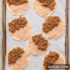 Several small flour tortillas laid out, each spread with a layer of refried beans and topped with the seasoned ground beef mixture, ready for folding.
