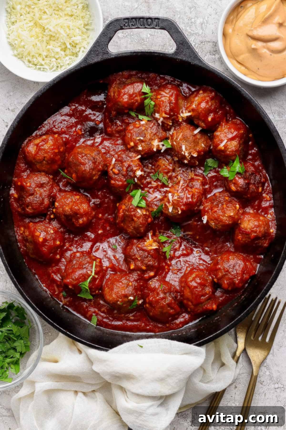 Hearty Sloppy Joe Meatballs 2 A cast iron skillet filled with glossy, saucy sloppy joe meatballs, garnished with fresh parsley, surrounded by small bowls of grated cheese, extra sauce, and chopped herbs ready for serving.