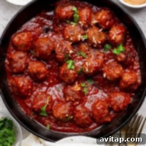 A cast iron skillet filled with meatballs in tomato sauce, garnished with parsley, surrounded by bowls of grated cheese, sauce, and chopped herbs.