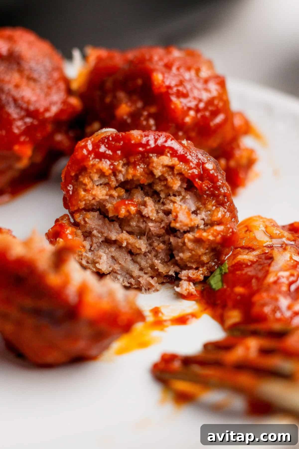 Hearty Sloppy Joe Meatballs 4 A close-up of a serving of sloppy joe meatballs generously covered in rich tomato sauce, with one meatball sliced open to reveal its tender, flavorful interior, presented on a pristine white plate.