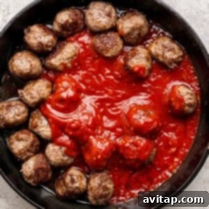 A cast iron skillet filled with meatballs arranged around a pool of tomato sauce on a light textured surface.