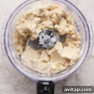 A food processor filled with partially mixed dough sits on a light-colored countertop.