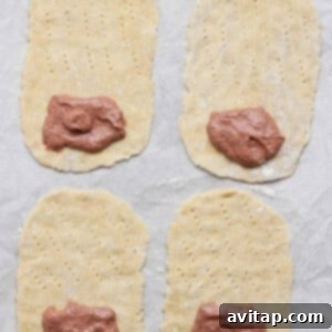 Four rectangular dough pieces, each with fork marks and a portion of meat paste on one end, are arranged on a parchment-lined surface.