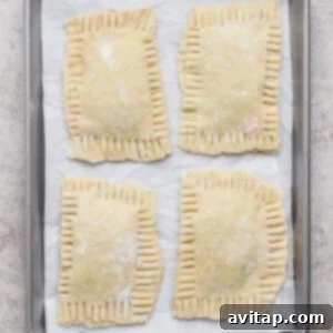 Four unbaked rectangular hand pies with crimped edges are arranged on a parchment-lined baking sheet.