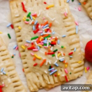 Rectangular pastry with icing and colorful sprinkles, surrounded by fresh strawberries on a white surface.