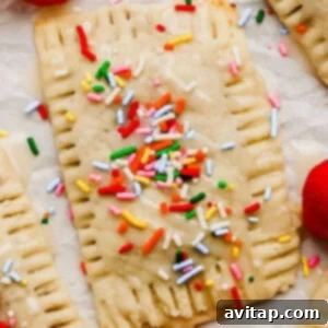 A rectangular pastry topped with icing and colorful sprinkles sits on parchment paper next to a fresh strawberry.