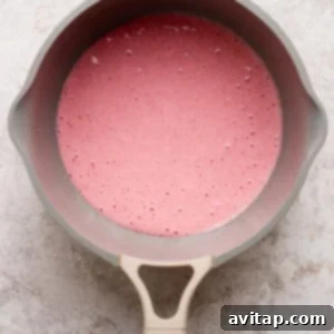 A beige saucepan filled with a pink liquid mixture sits on a light textured surface, viewed from above.