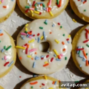 A close-up of vanilla-frosted donuts topped with colorful sprinkles arranged on parchment paper.