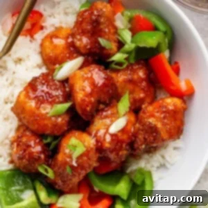 A bowl of white rice topped with crispy glazed chicken pieces, sliced green onions, and red and green bell peppers.