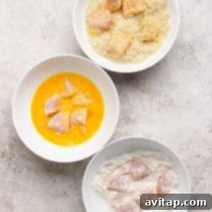 Three white bowls with raw chicken pieces: one with flour, one with beaten egg, and one with breadcrumbs, showing the breading process.