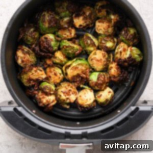 Addictive Chili Crunch Brussels Sprouts 8 Halved Brussels sprouts cooked in an air fryer basket, showing a browned, crispy texture on a light gray countertop.