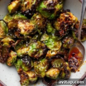 Addictive Chili Crunch Brussels Sprouts 9 A bowl of roasted Brussels sprouts topped with sesame seeds and chili oil, with a spoon on the side.