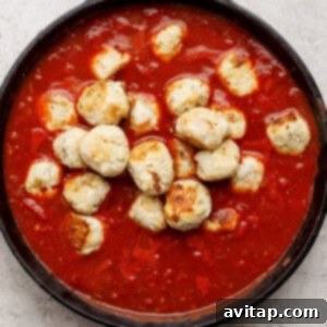 A cast iron skillet filled with meatballs in tomato sauce on a light textured surface.