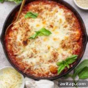 A cast iron skillet filled with baked cheesy tomato dish, garnished with fresh basil, surrounded by small bowls of shredded cheese and breadcrumbs.