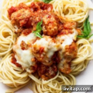 A plate of spaghetti topped with meatballs, tomato sauce, melted cheese, and garnished with fresh basil leaves.