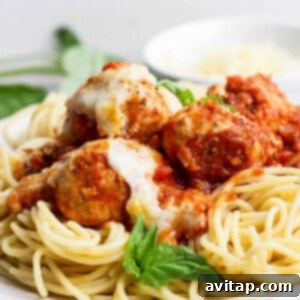 A plate of spaghetti topped with tomato sauce, meatballs, melted cheese, and a fresh basil garnish.