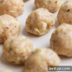 Raw chicken meatballs with visible herbs and cheese pieces arranged on a white plate, ready to be cooked.