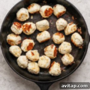 Cooked meatballs are arranged in a black cast iron skillet on a light textured surface.