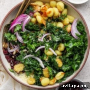 A bowl of salad with gnocchi, kale, red onion, dried cranberries, and grated cheese, with small bowls of pumpkin seeds and more cranberries on the side.