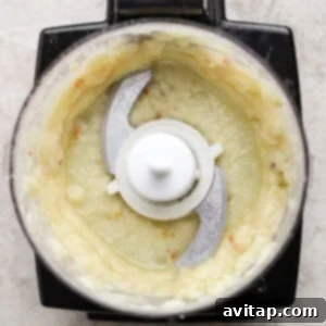 Top view of a food processor containing a pale, creamy blended mixture with visible metal blades in the center.