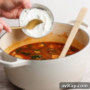 A person pouring cream into a pot of soup.
