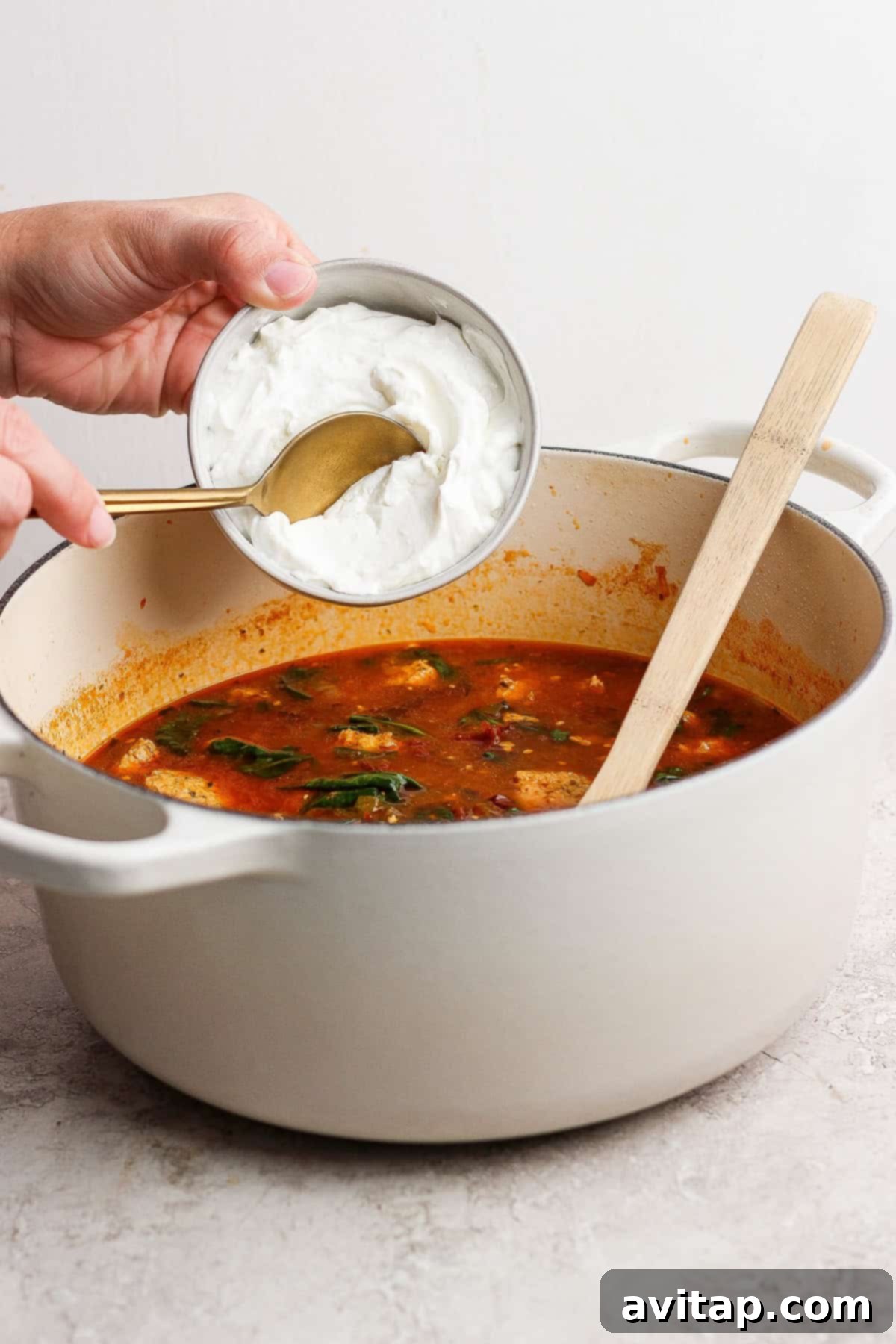 A person pouring cream into a pot of soup.