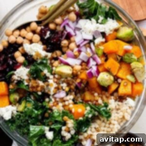 A vibrant couscous salad recipe featuring chickpeas, kale, roasted butternut squash, Brussels sprouts, Israeli couscous, red onion, dried cranberries, lentils, and crumbled cheese served with utensils.