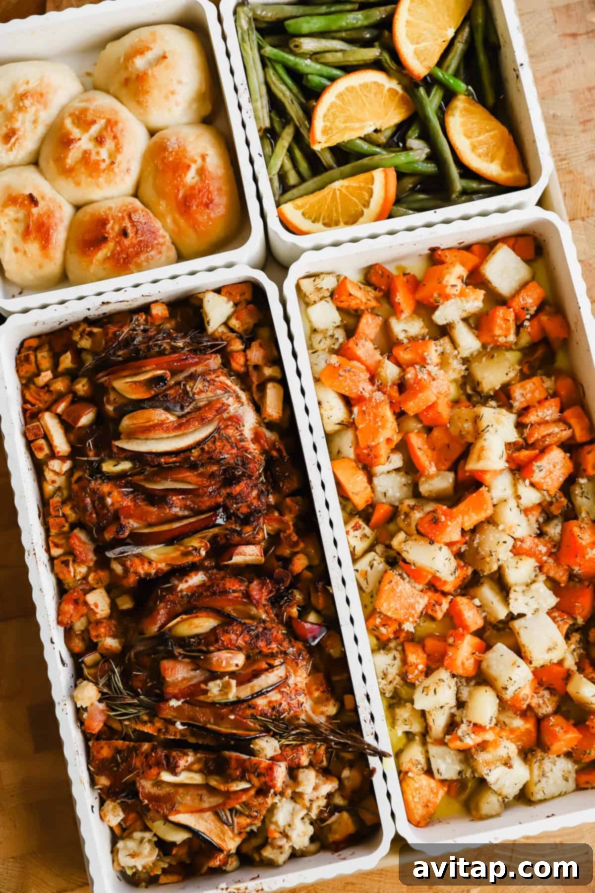 Four trays of food including dinner rolls, green beans with orange slices, roasted meat with herbs and vegetables, and a mix of roasted potatoes and carrots.