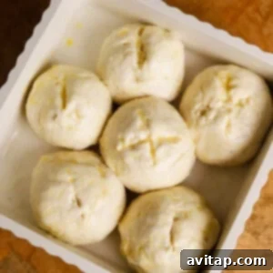 Six unbaked dough balls evenly arranged in a white baking dish, placed on a wooden surface.