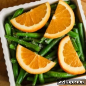 A white dish filled with green beans, topped with four orange slices, set on a wooden surface.