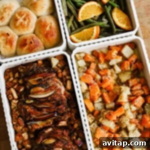 Four containers hold dinner rolls, green beans with orange slices, roasted meat with onions, and roasted potatoes with carrots.