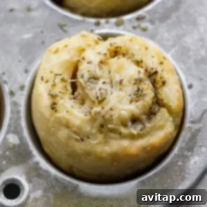 A baked pastry roll topped with melted cheese and herbs sits in a metal muffin tin, showing the finished product after baking.