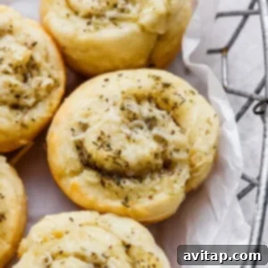 Close-up of savory pastry rolls topped with shredded cheese and herbs, arranged in a metal basket lined with white parchment paper, ready to be served.