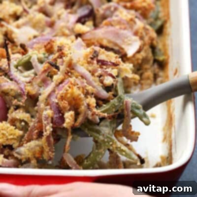 A hearty and comforting green bean casserole, beautifully baked in a white ceramic dish, crowned with a golden-brown, irresistibly crispy onion crust. It is invitingly ready to be served and enjoyed at a festive meal.