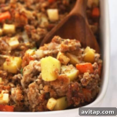 A rich and savory sausage stuffing, baked to a beautiful golden perfection in a pristine white casserole dish, with a rustic wooden spoon resting gently beside it. This inviting dish is ready to be served at a festive meal.