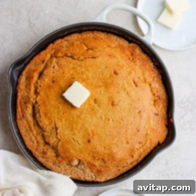A perfectly baked, rustic cornbread in a cast-iron skillet, beautifully displaying a golden-brown crust and a moist, inviting texture. The cornbread is ready to be sliced and served, promising homemade comfort and warmth.