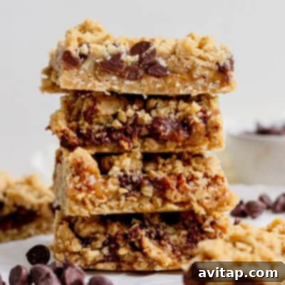 A delectable stack of four chocolate chip oatmeal bars, featuring a rich, crumbly texture and generously studded with abundant chocolate chips. The bars are presented on a white surface, with scattered chocolate chips for added visual appeal and an inviting hint of sweetness.