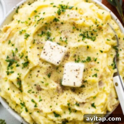 A generous, inviting bowl of whipped mashed potatoes, visibly creamy and luxurious, generously sprinkled with vibrant fresh herbs and featuring a luscious, melted pat of butter on top. It is invitingly ready to be served and savored.