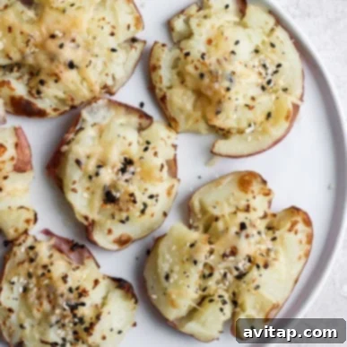 Perfectly smashed red potatoes, their skins crisply roasted to a golden hue, meticulously seasoned with aromatic herbs and a generous sprinkle of finely grated Parmesan cheese, elegantly presented on a white plate, invitingly ready to be thoroughly enjoyed.