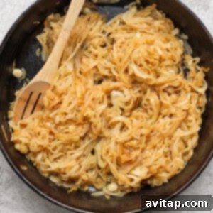 Sliced onions caramelizing in a black cast iron skillet with a wooden spoon resting on top.
