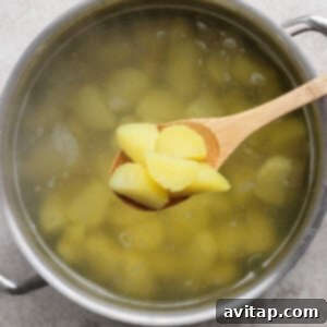 A pot of boiling water with peeled potato pieces, with several pieces being lifted out on a wooden spoon.