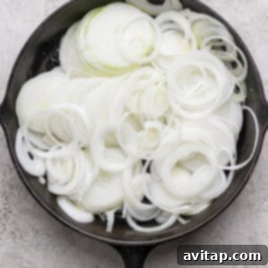 A cast iron skillet filled with raw, sliced white onions, arranged in overlapping rings on a light textured surface.