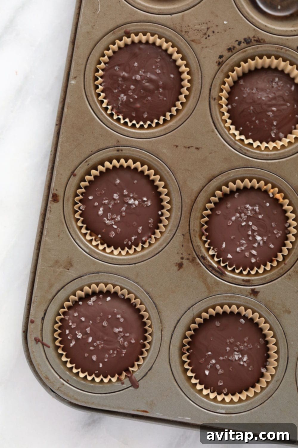 Homemade almond butter cups are a simple dessert that will satisfy your sweet tooth craving! Plus, these almond butter cups are topped with flakey sea salt. close-up of almond butter cups in a muffin tin, showing the distinct layers