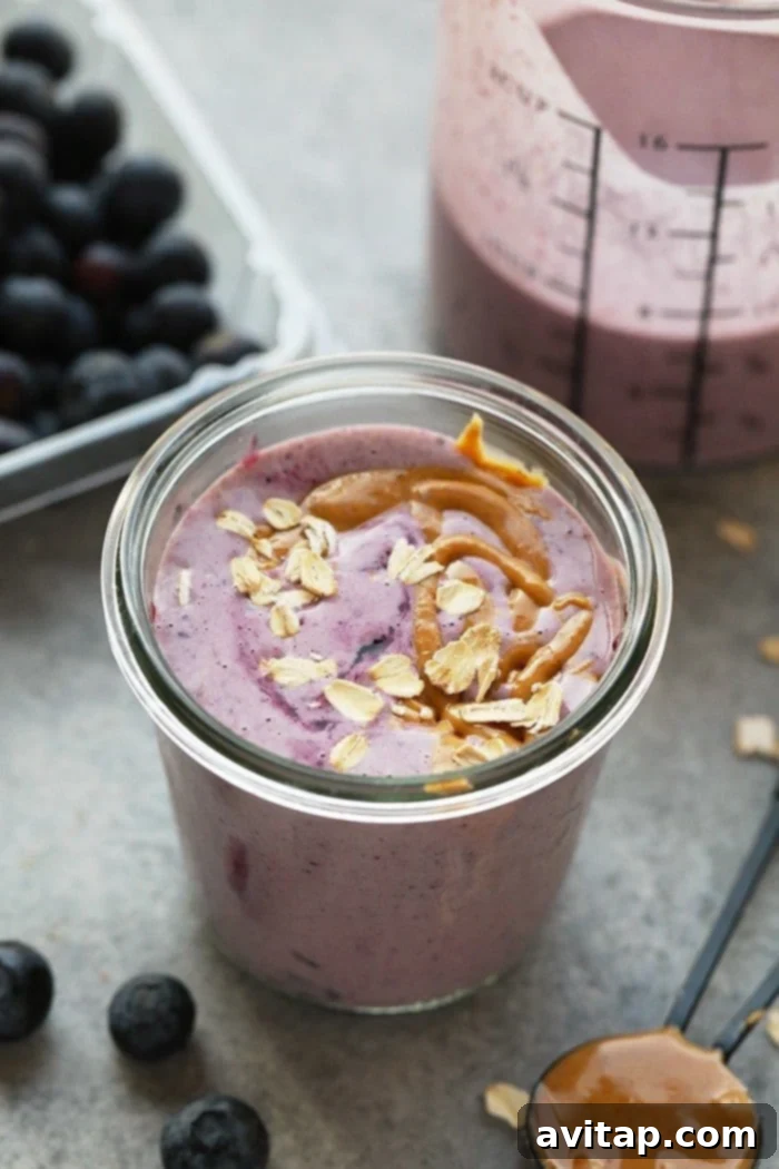 Peanut butter and jelly smoothie in a tall glass, garnished with berries.
