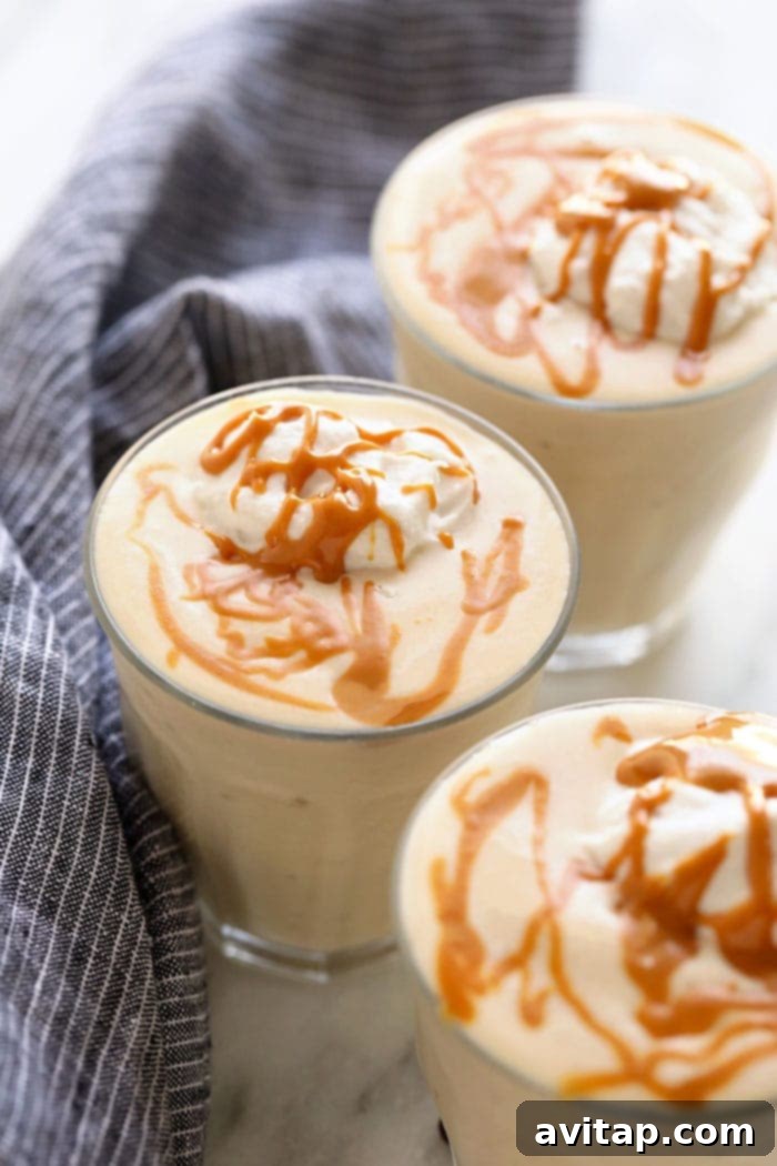 This Healthy Banana Protein Shake is packed with a short list of real ingredients and blended together to perfection! Boasting 16 g of protein per serving and oh so flavorful, this protein shake recipe will fuel your body post-workout or or as a sweet treat. Enjoy! A tall glass filled with a creamy healthy banana protein shake, garnished with a drizzle of peanut butter and a banana slice, sitting on a light-colored surface.