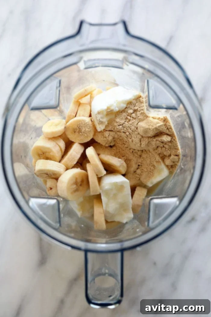 This Healthy Banana Protein Shake is packed with a short list of real ingredients and blended together to perfection! Boasting 16 g of protein per serving and oh so flavorful, this protein shake recipe will fuel your body post-workout or or as a sweet treat. Enjoy! Ingredients for a healthy banana protein shake, including frozen bananas, Greek yogurt, milk, and protein powder, neatly arranged inside a high-speed blender.