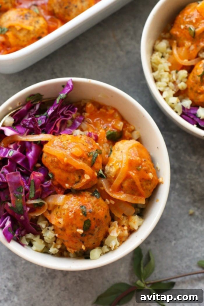 Vibrant Red Coconut Curry Meatballs with Cauliflower Rice in a bowl, garnished with fresh herbs.