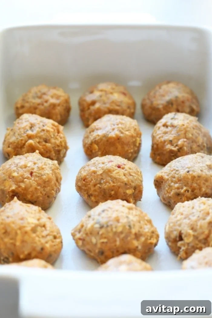 Golden-brown meatballs simmering in a rich curry sauce in a baking dish, ready for the oven.