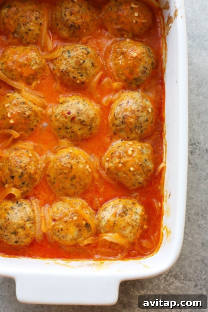 Close-up of juicy curry meatballs generously coated in rich red curry sauce, garnished with fresh cilantro.